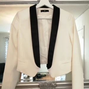 Vit kavaj med svart satin krage  - Snygg vit kavaj med kontrasterande svart satin krage (påminnerom Ralph Lauren). Croppad modell med stilren design och diskreta fickor framtill. Perfekt för dig som vill sticka ut med en klassisk men modern look. Materialet känns mjukt och har en lätt struktur.