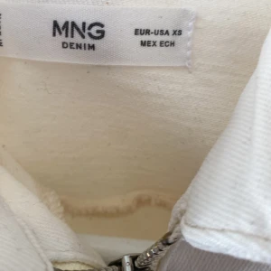 Vit jumpsuit med dragkedja från MNG Denim - Snygg vit jumpsuit från MNG Denim i storlek XS. Modellen har korta ärmar, krage och raka ben. Framtill finns en silverfärgad dragkedja och praktiska fickor. Materialet är kraftig bomull, perfekt för en cool och avslappnad look.