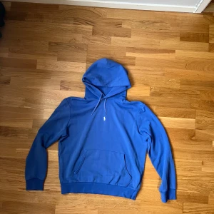 Blå hoodie från Polo Ralph Lauren, Skicka offer/Send offer - Snygg blå hoodie från Polo Ralph Lauren med klassisk huva och snörning. Tröjan har en liten vit logga på bröstet och en stor magficka framtill. Tillverkad i mjuk bomull, perfekt för chill dagar. Långärmad och med ribbade muddar för extra komfort.