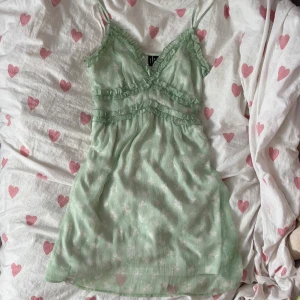 Grön blommig klänning - Supersöt ljusgrön klänning med vita blommor från Vero Moda i storlek XS men passar även S med mindre byst. Klänningen har tunna reglerbara axelband, v-ringad omlottfront och volangdetaljer över byst och midja! Knappt använd (färgen på sista bilden är mest verklighetstrogen)!💞