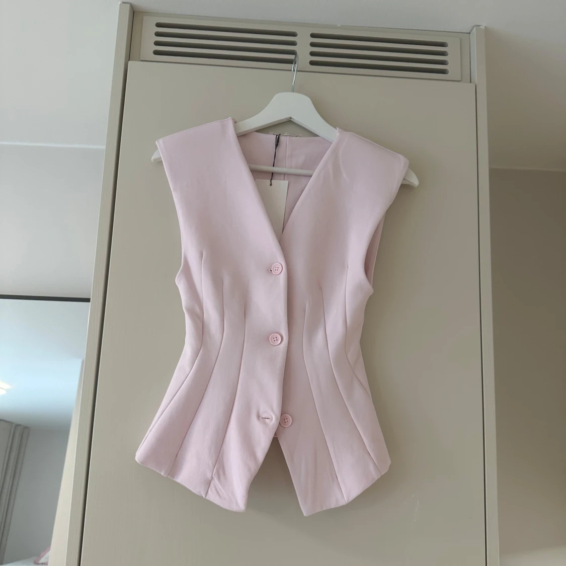 Ljusrosa figursydd väst med knappar