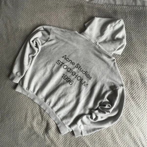 Grå hoodie från Acne Studios L - Säljer en clean grå hoodie från Acne Studios i storlek L. Tröjan har huva, långa ärmar och tryck med 'Acne Studios STOCKHOLM 1996' på ryggen. Tillverkad i 100% bomull för skön och mjuk känsla. Perfekt för chill dagar och streetwear vibes. Vid snabb affär kan priset ändras!