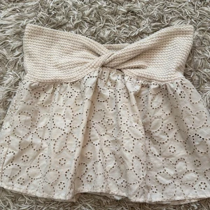 Beige tubtopp med spets  - Superfin beige tubtopp från SHEIN med virkad bandeau upptill och broderad spets med blommönster nedtill. Toppen är axelbandslös och har en twistad detalj framtill. Perfekt för sommarens alla häng och ger en söt vibe till din outfit.