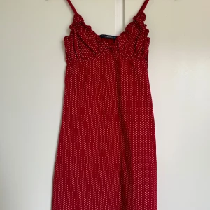 Röd prickig linne Brandy Melville - Supersöt röd kortklänning från Brandy Melville med vita prickar och volangdetaljer vid axelbanden. Klänningen är ärmlös med smala axelband och har en lätt A-linjeformad siluett. Materialet är mjuk bomull, perfekt för varma dagar och en chill vibe.