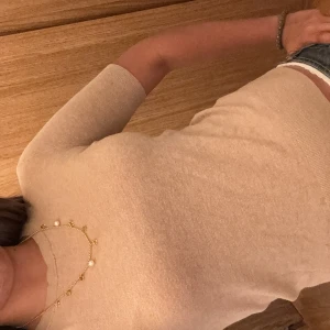 Beige stickad tröja från Zara - Säljer en beige stickad tröja med korta ärmar och rund hals. Tröjan har snygga knappar bak i nacken och ribbade muddar vid ärmslut. Passar dig som gillar neutrala färger och mjuka material. Har ett litet hål k kragen på baksidan men det går lätt att fixa!!