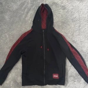 Svart hoodie från Hugo med röda detaljer - Säljer min Hugo kofta som är i mycket bra skick /knappt använd storleken på koftan är s. Pris kan diskuteras vid snabb affär 