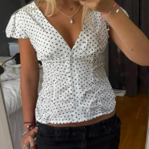 Vit prickig blus  - Säljer en söt vit blus med svarta prickar och v-ringad hals. Blusen har korta puffärmar och knappar framtill. Aldrig använd💞