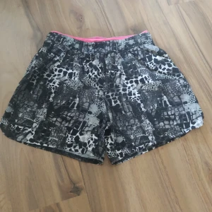 Svarta träningsshorts med leopardmönster från SOC - Snygga träningsshorts från SOC med svart och vit leopardmönstrad design. De har en elastisk midja med rosa SOC-logga och snörning för extra komfort. Materialet är lätt och passar perfekt för aktiva dagar. Shortsen har loose passform och coolt mönster som sticker ut.
