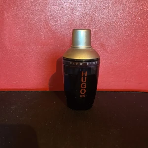 Hugo Boss Dark Blue parfym - Hugo Boss Dark Blue parfym i en stilren mörkblå flaska med guldfärgat lock. Flaskan har en modern, rundad form och tydlig logga i orange. Perfekt för dig som gillar klassiska och maskulina dofter.
