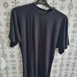 Svart basic t-shirt i bomull - En svart, enkel t-shirt med rund hals och korta ärmar. Modellen är loose fit och tillverkad i mjuk bomull, perfekt för en chill och avslappnad stil. Passar dig som gillar minimalistiskt och cleant uttryck.