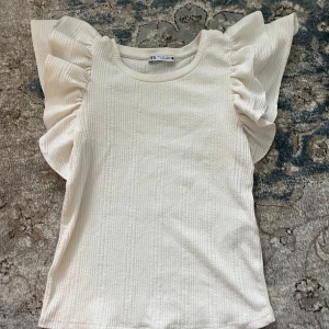 Sommartopp från Zara - En jättesöt cremevit sommartopp med volanger från Zara! Nästan aldrig använd så i väldigt bra skick. Stl S. 