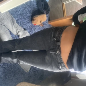 Svarta bootcut jeans från Gina Tricot  - Säljer ett par svarta jeans från Gina Tricot i bootcut-modell. De har låg midja, klassiska fem fickor och snygga detaljer med knappar på bakfickorna. Jeansen är gjorda i ett mjukt denim-material som sitter skönt och har en stilren look.