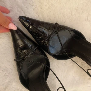 Svarta spetsiga Gucci klackar  - Säljer ett par svarta klackar från Gucci med spetsig tå och låg klack och tunna snören som går över foten. Perfekta för dig som gillar en edgy och elegant look. Nypris runt 8000kr