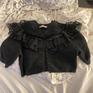 Zara bolero - Supersnygg svart bolero från Zara med volangdetaljer och spets upptill. Croppad modell med knappar framtill och långärmad. Perfekt för dig som gillar statement-plagg med coola detaljer och vill sticka ut lite extra.