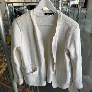 Vit kofta från Gina Tricot XS - Snygg vit kofta från Gina Tricot i storlek XS. Den är stickad med mjukt material, har två praktiska fickor framtill och långärmade ärmar. Perfekt att slänga över en t-shirt för en chill look. Enkel, stilren och passar till allt.