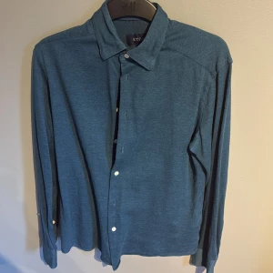 Blå skjorta från Eton, storlek M - Snygg blå skjorta från Eton i storlek M. Skjortan har klassisk krage, vita knappar och lång ärm. Materialet känns mjukt och har en lätt struktur, perfekt för dig som gillar stilrena plagg med enkel design.