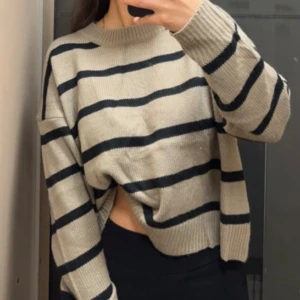 Beige och svart randig stickad tröja - Säljer en beige stickad tröja med svarta horisontella ränder. Tröjan har en loose passform, rund hals och långa ärmar med ribbade muddar. Perfekt för dig som gillar chill och avslappnad stil.