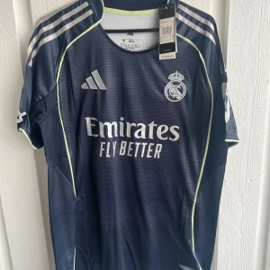 Real Madrid Mbappé #10 fotbollströja - Snygg marinblå Real Madrid fotbollströja från Adidas med Mbappé och nummer 10 på ryggen. Tröjan har vita detaljer, silverfärgade Adidas-ränder på axlarna och klubbmärke på bröstet. Tillverkad i lätt funktionsmaterial med korta ärmar och UEFA Foundation-märke på ärmen.