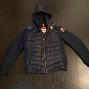 Mörkblå pufferjacka från Parajumpers - Snygg mörkblå pufferjacka från Parajumpers med huva och  PJS-märke på ärmen. Materialet är polyester och jackan har en normal passform med långärmade ärmar. Pris kan diskuteras