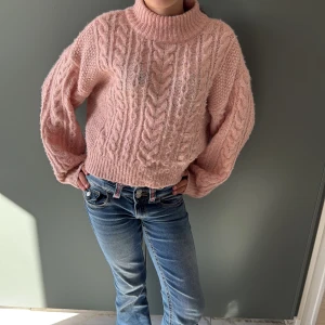 Rosa stickad polotröja från ONLY - Supermysig rosa polotröja från ONLY med grovstickat flätmönster och ribbade muddar. Tröjan har en loose passform, lång ärm och hög krage som ger extra cozy vibe. Perfekt för kyliga dagar och att styla med jeans eller kjol.