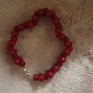Rött glittrigt pärlarmband - Snyggt armband med röda glittriga pärlor som är trädda på rad och har ett silverfärgat lås. Perfekt för dig som gillar färgstarka accessoarer och vill sticka ut lite extra. Pärlorna är runda och har en skimrande yta som fångar ljuset.