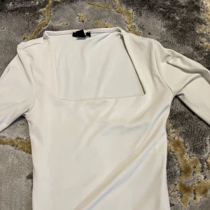 Vit långärmad topp från Amisu - Snygg vit långärmad topp från Amisu i storlek S. Toppen har en fyrkantig halsringning som ger en modern vibe och är gjord i ett mjukt, stretchigt material som sitter skönt mot kroppen. Perfekt att styla med jeans eller kjol för en clean look.