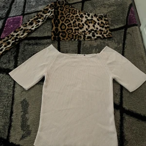 Leopardmönstrad one shoulder topp och en rosa topp. Storlek XS.  - Säljer en riktigt cool one shoulder topp med leopardmönster i brunt, beige och svart. Toppen har en lång ärm och är croppad, perfekt för att sticka ut. Materialet känns mjukt och stretchigt, så den sitter snyggt på kroppen. Och en snygg vit t-shirt/topp som är öppen vid axlarna eller att det hänger ner vid axlarna. Båda i storlek XS. 
