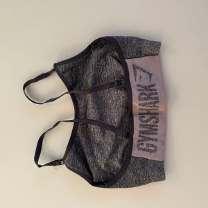 Grå sporttopp från Gymshark - Säljer en grå sporttopp från Gymshark med justerbara axelband. Toppen har en bekväm passform och är perfekt för träning. Den har en elastisk kant med Gymshark-loggan i svart.