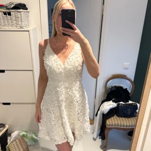 Vit blommig klänning, studentklänning - Säljer en superfin vit klänning med blommigt mönster och smala axelband. Klänningen har en v-ringad design och är perfekt för studenten och sommaren.. Den är kort och har en dragkedja i ryggen för enkel påklädning. Har använt den 1 gång på min egna student så den är i nyskick! Nypris var cirka 1500kr