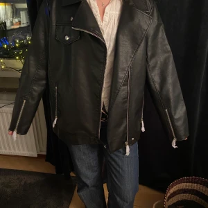 Svart skinnjacka med dragkedja - Säljer en svart skinnjacka med coola dragkedjedetaljer. Jackan har en oversized passform och långa ärmar. Den känns mer som en M i storleken.