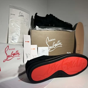 Svarta sneakers med nitar från Christian Louboutin - Snygga svarta sneakers från Christian Louboutin med ikoniska röda sulor. Skorna har en stilren design med nitar på tån och snörning. Perfekta för att ge en edgy touch till din outfit.