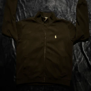 Ralph Lauren full zip  - Säljer en stilren svart tröja från Ralph Lauren med dragkedja och det klassiska logotypbroderiet på bröstet. Perfekt för en casual look. Problemet med tröjan är att den är liten i storlek dvs den sitter som S