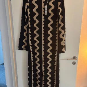 Svart och beige stickad klänning - Snygg svart och beige stickad klänning med vågigt mönster från NAKD. Aldrig använd med lappar kvar. Säljer då jag inte hann returnera. Nypris 799kr