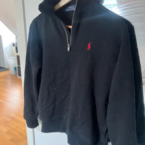 Svart hoodie från Ralph Lauren - Säljer en stilren svart hoodie från Ralph Lauren med dragkedja och det klassiska röda logotypen på bröstet. Perfekt för en avslappnad look. Passar bra till både jeans och joggers. 