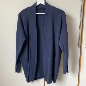 Åskblå kofta från Åhléns - Fin åskblå kofta från Åhléns i storlek M. Koftan är öppen utan knäppning. Det finns två små hällor i sidorna för ett tunnare skärp eller skinnsnöre. Rymlig. Skön, lite kraftigare kvalitet. Längd 80 cm. 