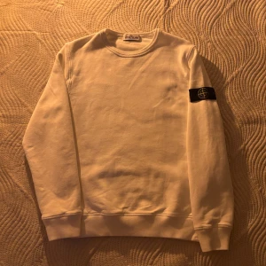 Vit tröja från Stone Island Junior 156 - Säljer en stilren vit tröja från Stone Island Junior. Tröjan har en rund halsringning och ett ikoniskt märke på armen. Perfekt för en avslappnad och trendig look. Har använt den några gånger.