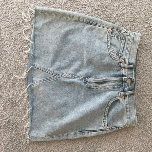 Jeanskjol med fransig kant - Snygg jeanskjol i ljusblå denim med fransig kant. Kjolen har klassiska femficksdetaljer och en bekväm passform. Perfekt för en avslappnad stil.