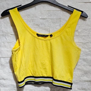 Gul linnetopp från Soul River - Säljer en solgul linnetopp från Soul River med svarta och vita ränder vid nederkanten. Perfekt för en färgglad och sportig look. Toppen är ärmlös och croppad, vilket gör den idealisk för varma dagar.