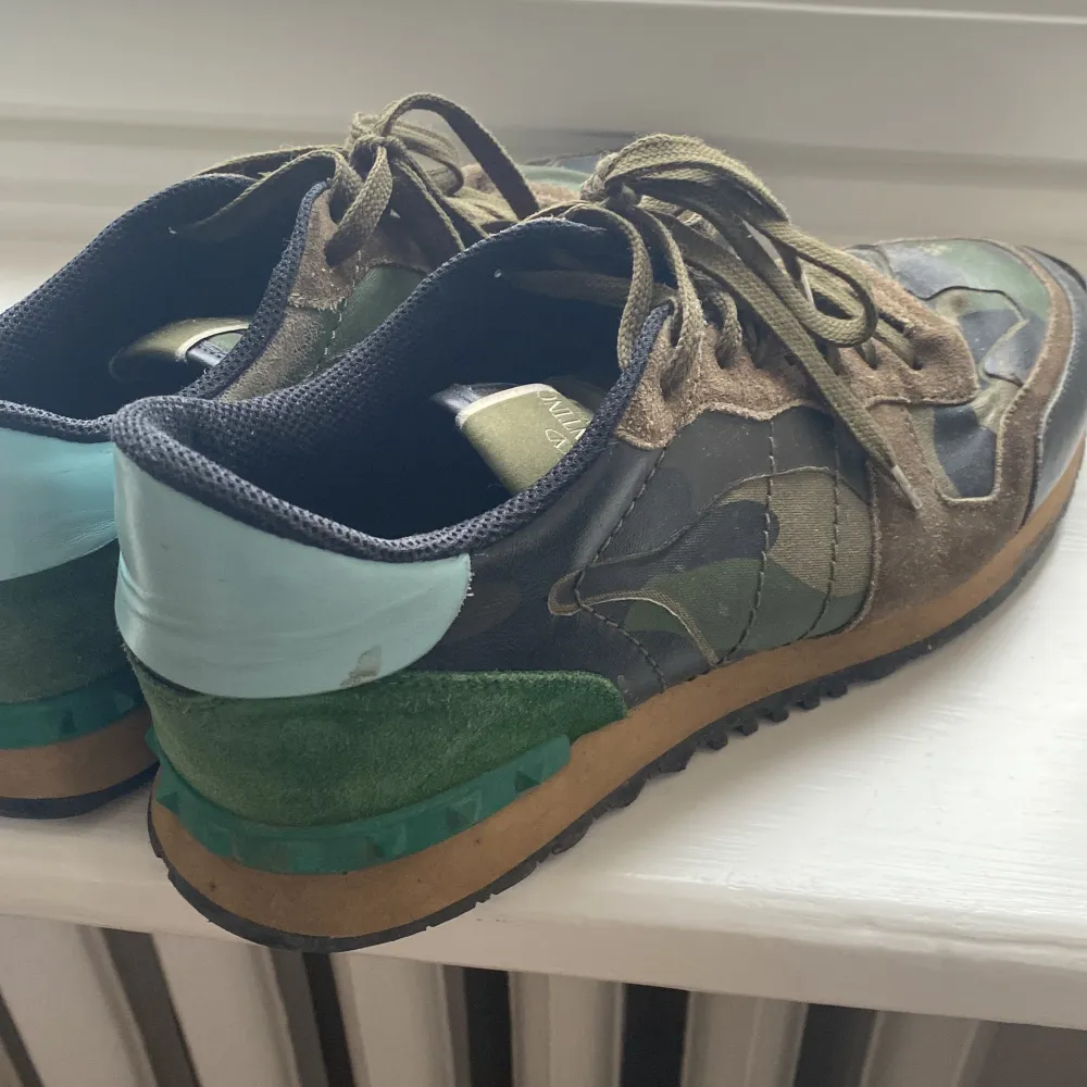 Snygga Valentino Rockrunner sneakers i ett coolt camouflage-mönster. Skorna har snörning och är tillverkade i en mix av mocka och syntetmaterial. De har en unik design med gröna detaljer på hälen.. Kengät.