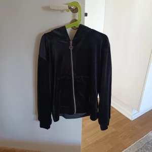 Svart sammetshoodie med dragkedja - Snygg svart hoodie i mjukt sammetstyg med dragkedja framtill. Perfekt för en avslappnad stil med en touch av lyx. Den har långa ärmar och en praktisk huva.