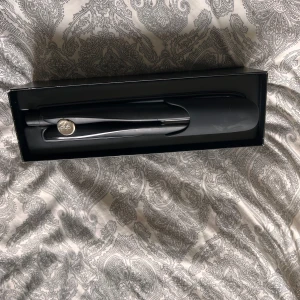 GHD gold plattång  - Säljer en elegant svart plattång från ghd. Perfekt för att skapa släta och glansiga frisyrer. Den har en stilren design med en rundad form och en silverdetalj med ghd-loggan. Kommer i originalförpackning. Använd fåtal gånger 