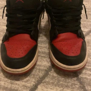 Nike Air Jordans i svart, röd och vit - Säljer ett par klassiska Nike jordans 1 low i svart, röd och vit, litet hål vid hälen på båda skorna, syns på bilden, men annars helt oskadd, använd upp till 10 gånger 