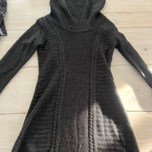 Svart stickad klänning från A. Byer - Säljer en svart stickad klänning från A. Byer med en mysig polokrage. Tröjan har långa ärmar och ett snyggt flätmönster längs sidorna. Perfekt för kyliga dagar!