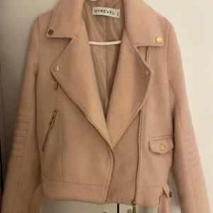 Rosa jacka från Ivyrevel - Snygg rosa jacka från Ivyrevel med dragkedja och guldiga detaljer. Jackan har en klassisk bikerstil med snedställd dragkedja och dekorativa knappar. Perfekt för att ge din outfit en trendig touch.