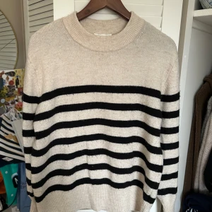 Beige och svart randig tröja från H&M - Säljer en snygg beige tröja med svarta ränder från H&M. Tröjan har en rund hals och långa ärmar, perfekt för en stilren look. Den är mjuk och bekväm, idealisk för kyligare dagar.