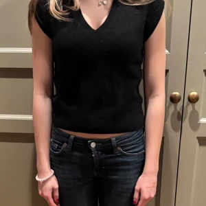 Svart kashmirtröja från Uniqlo - Säljer en elegant svart kashmirtröja från Uniqlo. Tröjan har en v-ringad design och korta ärmar, perfekt för en stilren look. Den är tillverkad i 100% kashmir vilket ger en lyxig och mjuk känsla. Passar perfekt för både vardag och speciella tillfällen.