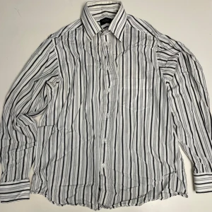 Randig skjorta från Randolph - Säljer en stilren vit och svart randig skjorta från Randolph. Skjortan har långa ärmar och knappar framtill. Perfekt för en klassisk look.