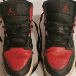 Svarta och röda Nike Air Jordans - Säljer ett par klassiska Nike Air Jordans i svart och rött. Skorna har snörning och den ikoniska Air Jordan-loggan på sidan. Perfekta för dig som älskar sneakers med stil och komfort.
