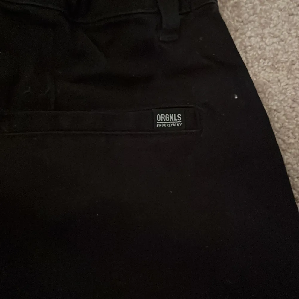Snygga svarta slim fit byxor från H&M med justerbar midja. Perfekta för en stilren look. Byxorna har en diskret etikett med texten 'ORGNLS BROOKLYN NY' vid bakfickan.. Farkut & Housut.