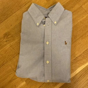 Blå skjorta från Ralph Lauren - Snygg blå skjorta från Ralph Lauren i bra skick. Den är i storleken S men den passar även på XS. Skjortan är i bra skick, men har en liten tråddragning på ryggen, detta visas på 5 bilden. 